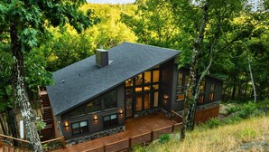 A modern cabin with a large deck, surrounded by trees.
