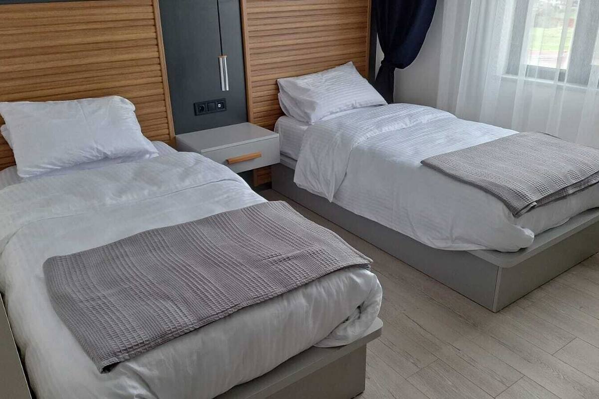 Una habitación de hotel con dos camas, una mesita de noche y un ventanal con cortinas.