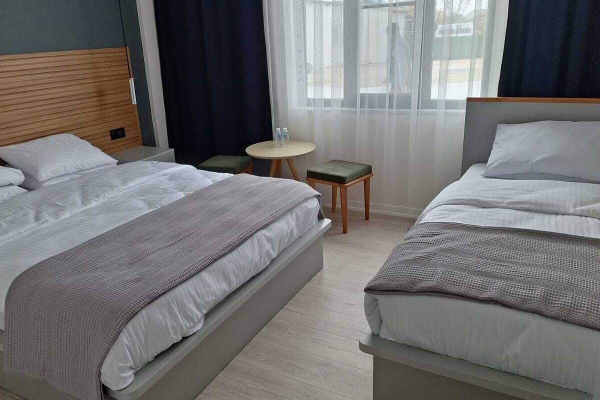Habitación de hotel con dos camas, una mesita redonda y un ventanal con cortinas.