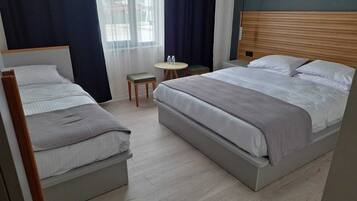 Habitación de hotel con dos camas, una mesita redonda y vistas al exterior a través de cortinas translúcidas.