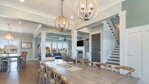 A spacious dining area with a large wooden table and wicker chairs, a chandelier, and a staircase leading to another level. - Barnacle Bill's: Private Pool w/dock & Ramp (Murrells Inlet)