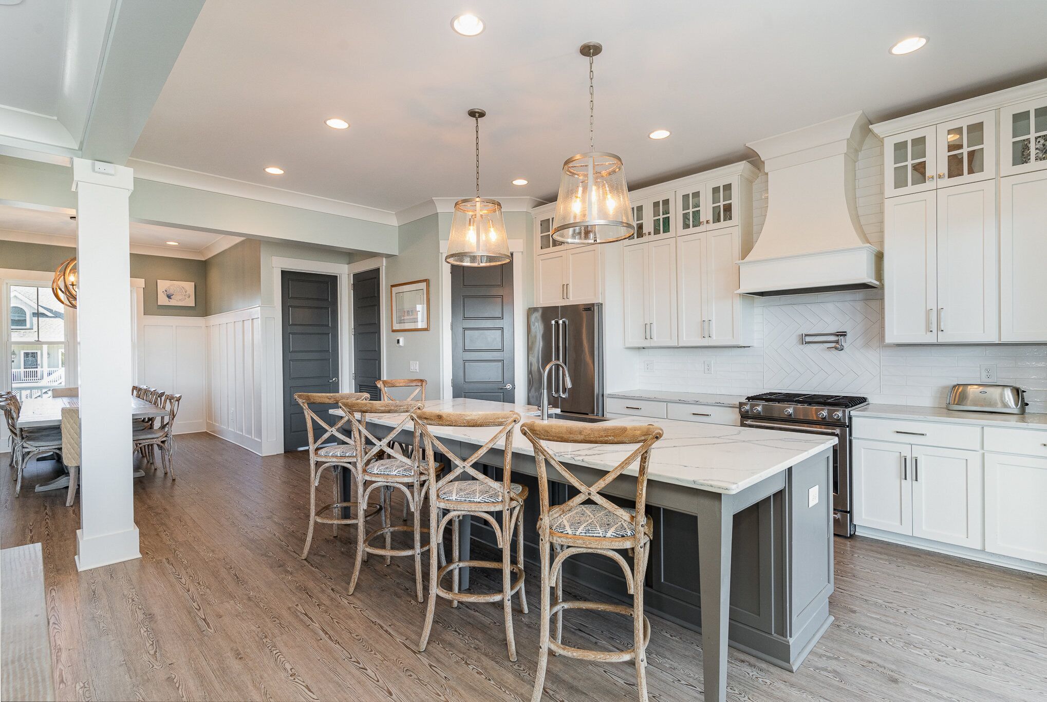A kitchen with white cabinets, a central island with bar stools, stainless steel appliances, and pendant lighting.