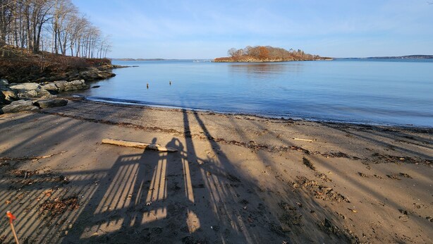 Ein Strand mit blauem Himmel, ruhigem Wasser und einer entfernten Insel.
