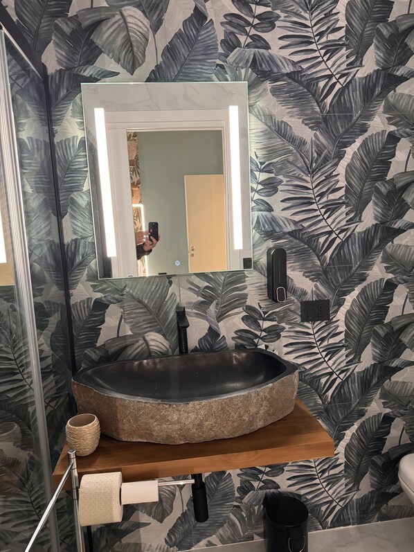 A bathroom with a round stone sink, a mirror with lights, a towel dispenser, and a toilet. - B&B Principe Amedeo (Taranto)