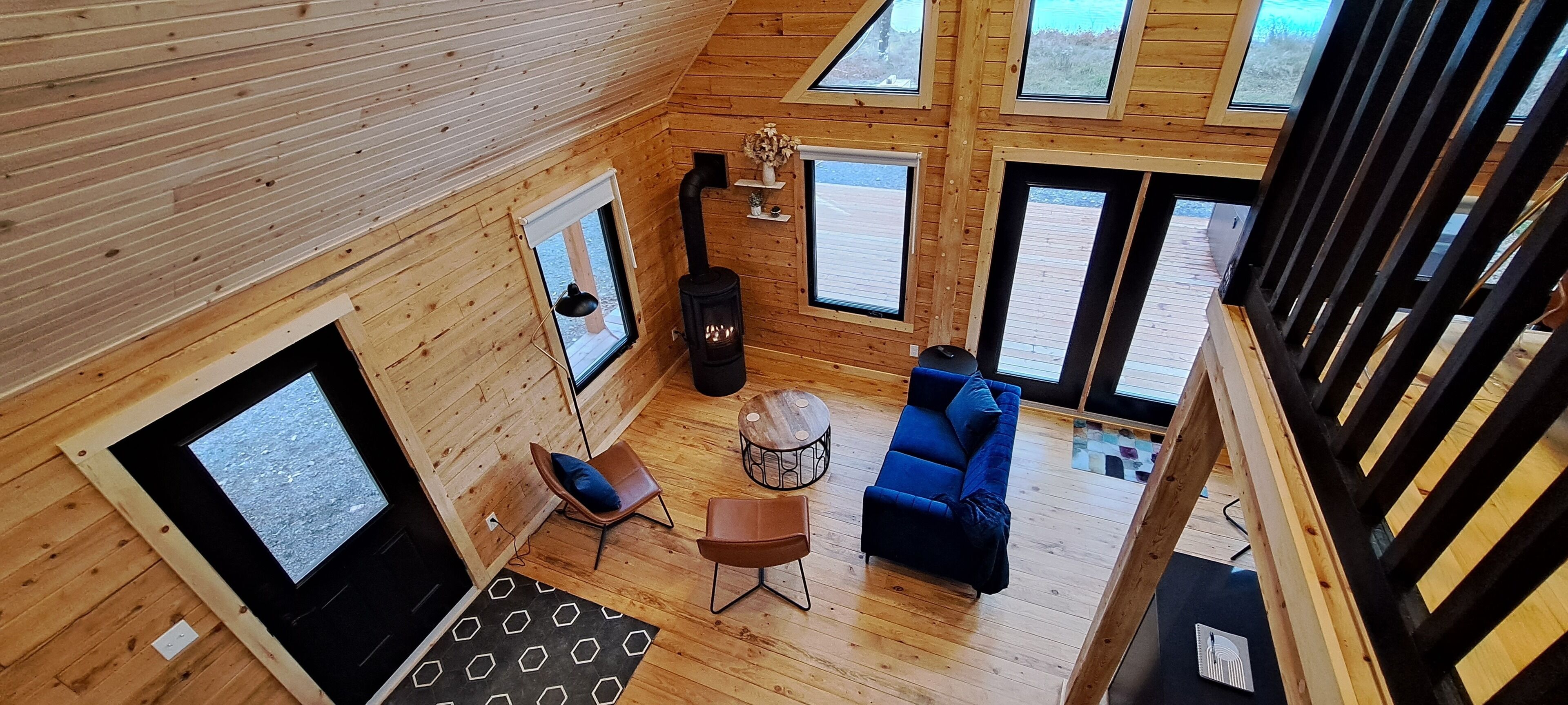 Een houten blokhut van binnen, met een bank, stoelen, een kleine tafel en een open haard.