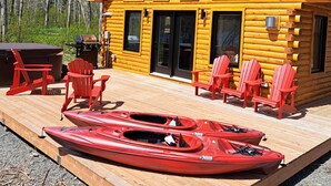 Una cabaña de troncos con terraza, sillas Adirondack rojas y kayaks rojos.