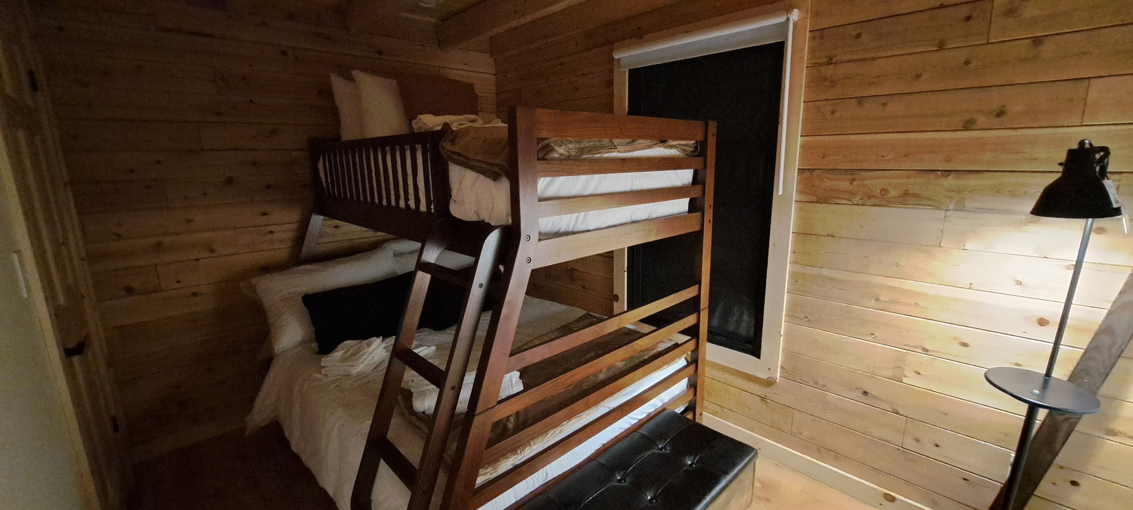A wooden cabin room with bunk beds, a window, and a lamp.