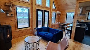Una cabaña con una sala de estar acogedora, que incluye un sofá azul, una mesa redonda y un estufa de leña.
