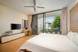A modern bedroom with a large bed, a desk, a TV, and a balcony with plants. - T P Deluxe Villa (Da Nang)