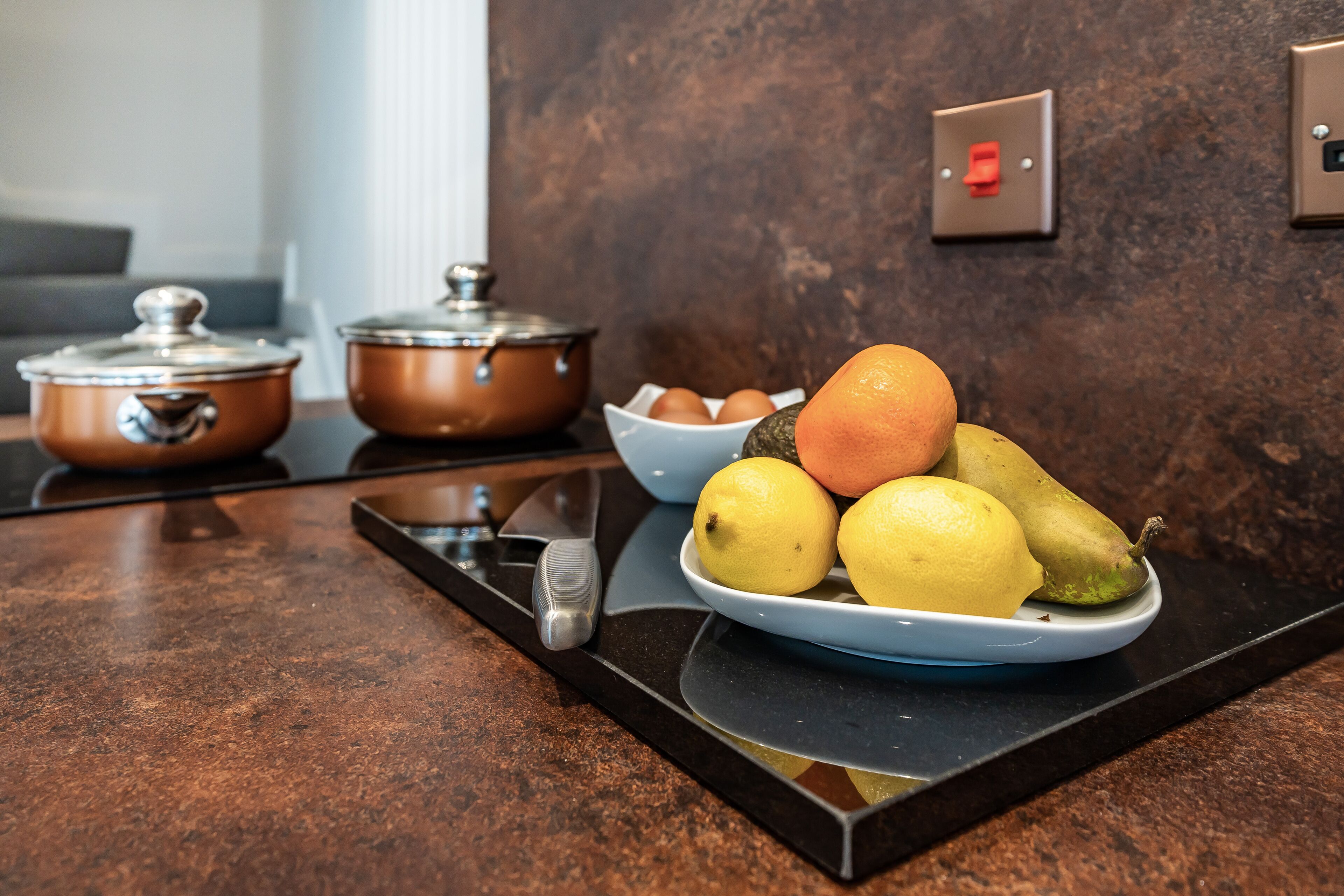 A kitchen counter with copper pots, a knife, and a plate of fruit.