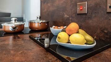 A kitchen counter with copper pots, a knife, and a plate of fruit.