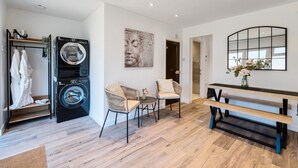 Een moderne wasruimte met een voorlader wasmachine en droger, twee rieten stoelen, een kleine tafel en een bank.