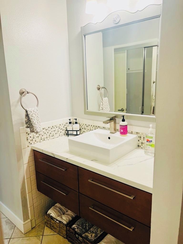 A bathroom with a white sink, dark wooden vanity, a large mirror, and a tiled backsplash.