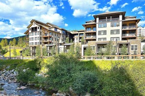 A multi-story hotel with balconies, a stone facade, and a river in the foreground.