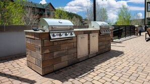 Een buitenkeuken met een barbecue en een ingebouwde oven, omringd door een bakstenen muur en een geplaveid terras.