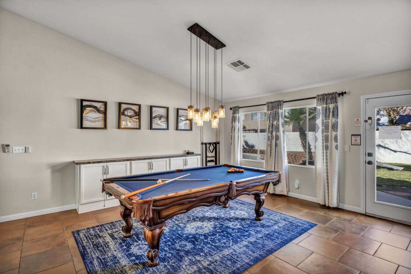 Een pooltafel in een ruimte met een groot raam, een plafondlamp en een deur met uitzicht op de omgeving.
