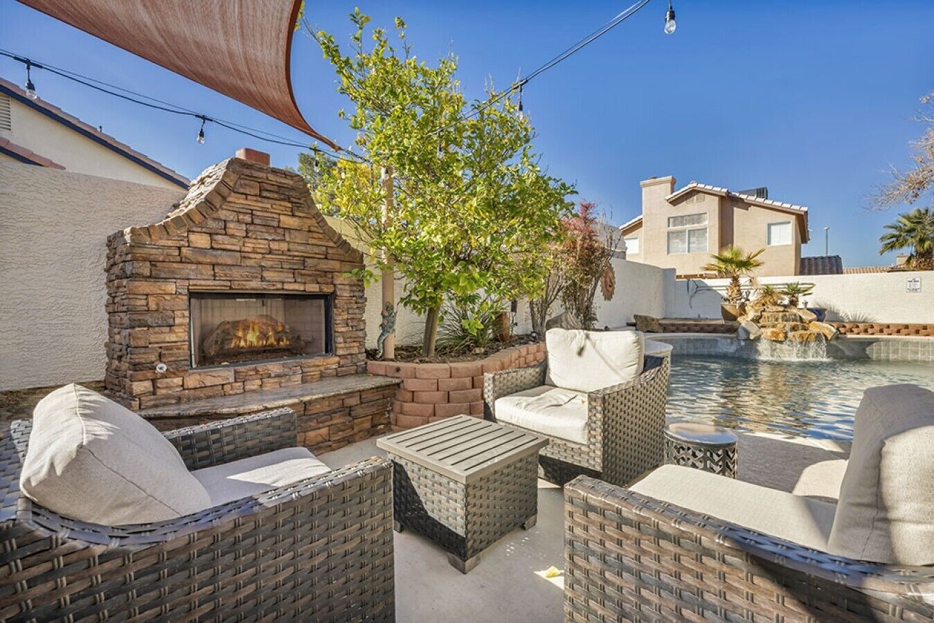 Un espace extérieur aménagé avec une cheminée en pierre, des meubles en osier et une piscine.