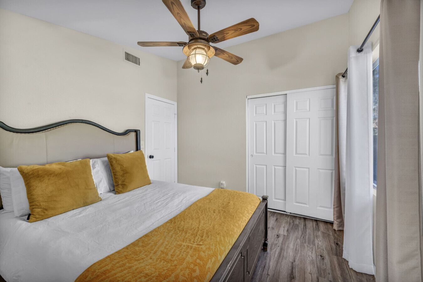 A bedroom with a bed, a ceiling fan, a wardrobe, and a window with curtains.