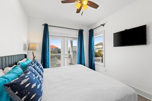 Camera d'hotel con un letto, una ventola a soffitto, una televisione e un balcone con tende blu.