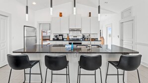 A modern kitchen with a central island, black bar stools, and pendant lighting. - Pool | Elevator | Sleeps 10 (Cape San Blas)