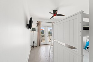 A room with a white ceiling fan, a mounted TV, a floor lamp, and a view of the outside through a glass door. - Pool | Elevator | Sleeps 10 (Cape San Blas)