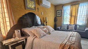 Un dormitorio con una cama grande, un sofá, una mesita de noche y un aire acondicionado instalado en la pared.