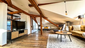 Un loft spacieux avec des poutres apparentes, une grande télévision, un canapé et un tapis à motifs.