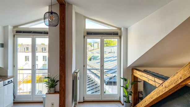 Une cuisine moderne avec de grandes fenêtres, un plafond en bois et une vue sur les bâtiments voisins.