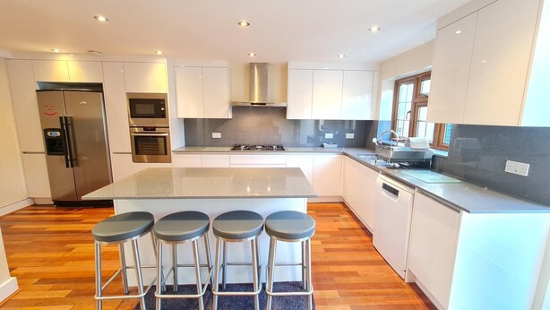 A modern kitchen with a central island, four bar stools, stainless steel appliances, and white cabinetry. - London Luxury House Sleeps 16 , Close to Tube, Free Parking, Garden,  Free Wifi (Ilford)