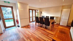 A modern kitchen with wooden flooring, a dining table with chairs, a refrigerator, and a fire extinguisher near the door. - London Luxury House Sleeps 16 , Close to Tube, Free Parking, Garden,  Free Wifi (Ilford)