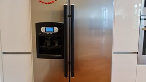 A stainless steel refrigerator with a digital display, located in a kitchen with white cabinets and a wooden floor. - London Luxury House Sleeps 16 , Close to Tube, Free Parking, Garden,  Free Wifi (Ilford)