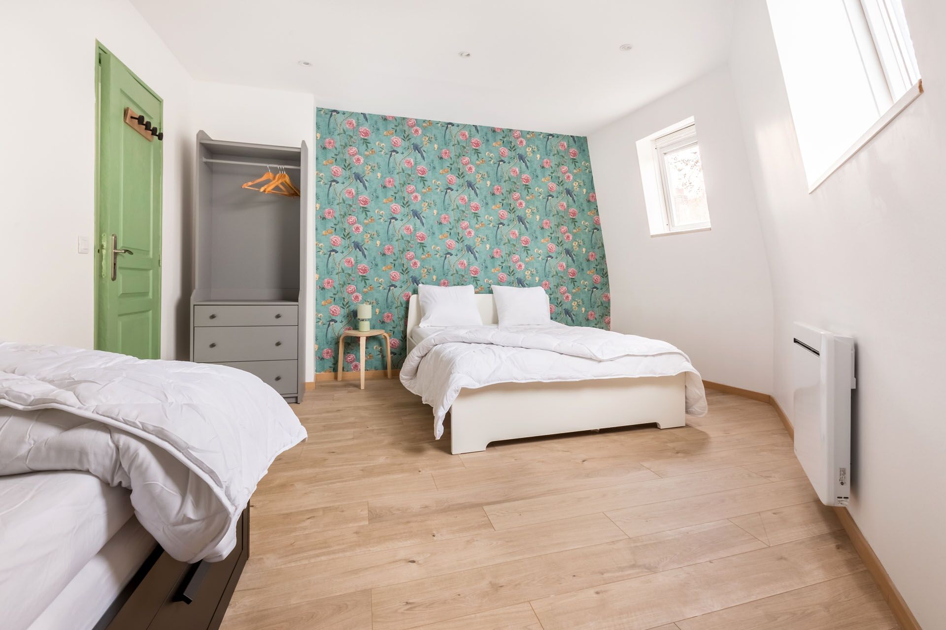 A bedroom with a bed, a dresser, a green door, and a floral wallpaper.