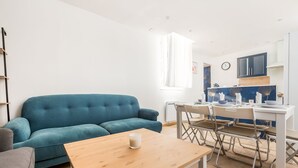 Una sala de estar moderna con un sofá azul, una mesa de centro de madera y un comedor con una mesa blanca y sillas de metal.