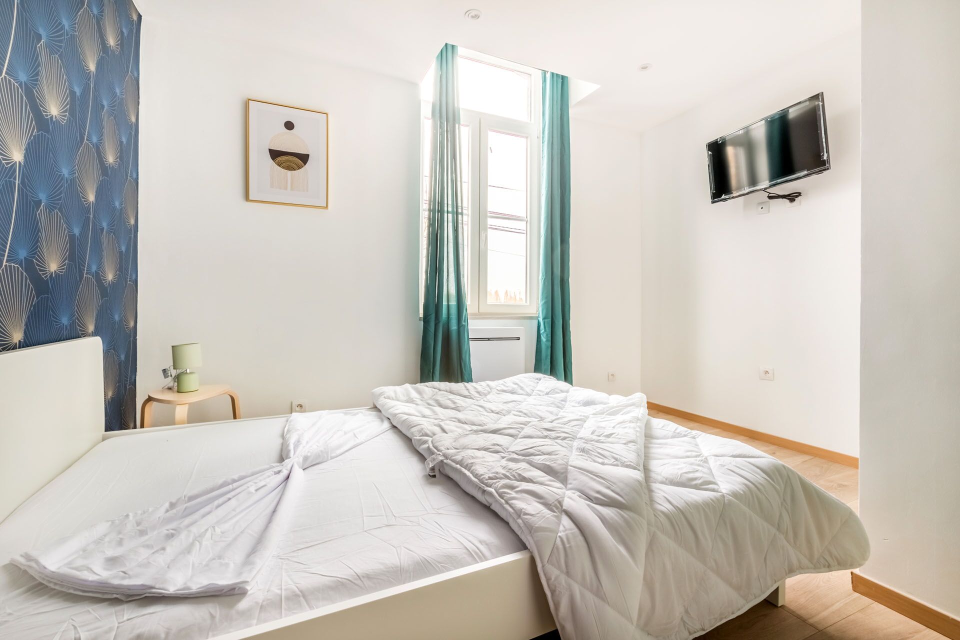 Une chambre à coucher avec un lit, un téléviseur fixé au mur et une fenêtre avec des rideaux.