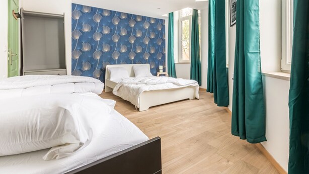 Un dormitorio con dos camas, una pared azul decorada con motivos de conchas marinas y cortinas verde agua.