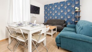 Una sala de estar con un sofá azul, un sillón gris y una mesa de comedor blanca dispuesta para cuatro comensales.