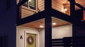 A two-story building with a visible entrance door, a balcony on the upper floor, and a light fixture above the door.