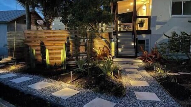 A modern house with a well-lit entrance, a wooden fence, and a gravel pathway leading to the door.