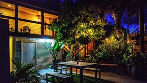 A patio area with a wooden table and benches, surrounded by potted plants and a large tree.