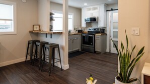 A modern kitchen with dark wood flooring, white cabinets, a microwave, oven, and a bar area with stools.