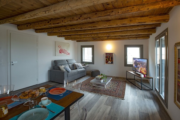 Una sala de estar con techo de madera, sofá gris, mesa de centro y televisor sobre un mueble.