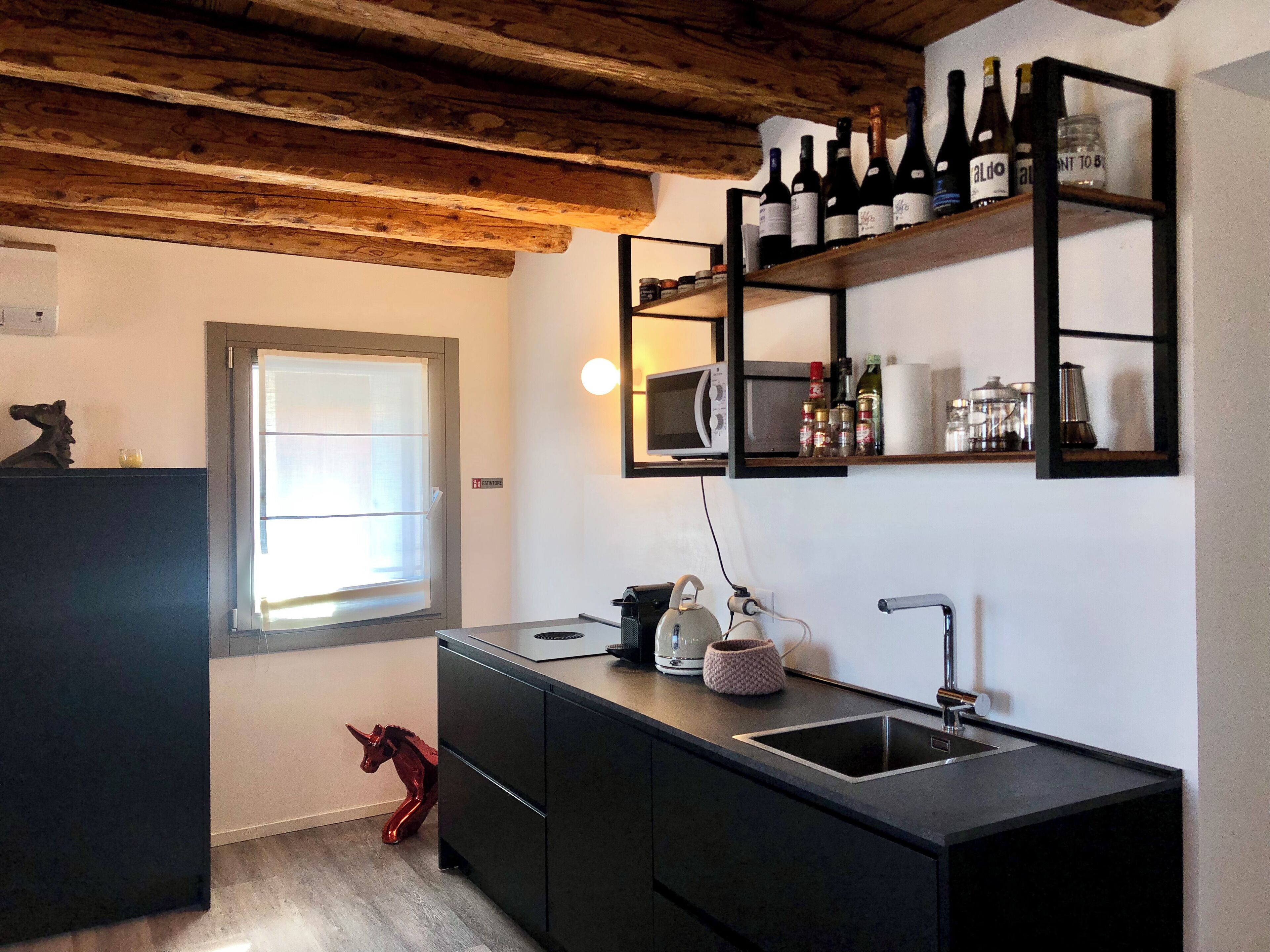 Una cucina moderna con mobili scuri, soffitto in legno, cella vinotecnica integrata e forno a microonde.