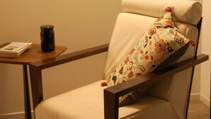 Una silla con un cojín floral, una obra de arte enmarcada en la pared y una mesita con un libro y un tarro.