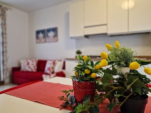 A living room with a red sofa, a coffee table, and two potted plants with yellow flowers. - Cozy Apartment With Swimming Pool (San Michele al Tagliamento)