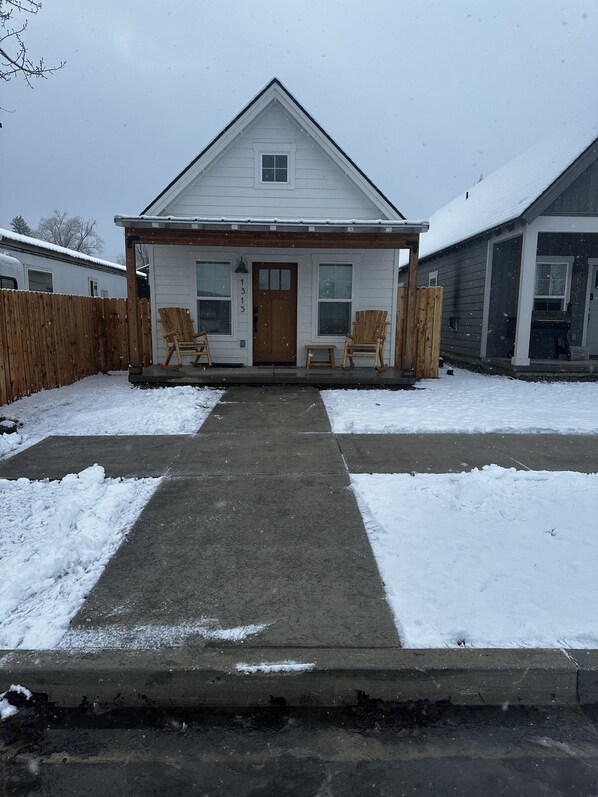 A single-story house with a front porch, two rocking chairs, and a wooden fence.