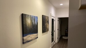 A hallway with two framed paintings on the wall, a door, and a lamp on a table in the background. - The Comfy Bear Cottage! Beautiful 2 bed/1bath home minutes from skiing and lake. (Sandpoint)