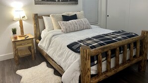 A bedroom with a wooden bed frame, white bedding, a plaid throw blanket, a bedside lamp, a small plant, and a framed picture on the wall. - The Comfy Bear Cottage! Beautiful 2 bed/1bath home minutes from skiing and lake. (Sandpoint)