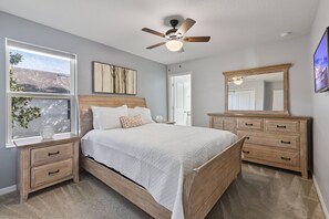 Un dormitorio con una cama de madera, un ventilador de techo, un ventanal con vistas y un aparador de madera.