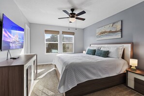 A bedroom with a bed, a ceiling fan, a TV, and a painting on the wall.