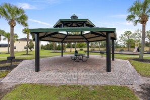 A covered picnic area with a table and benches, surrounded by palm trees and a brick pathway.